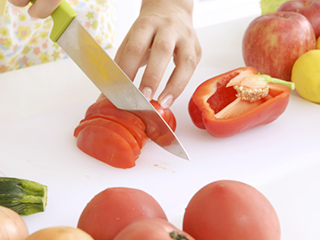 パプリカやリンゴなどが置かれたテーブルでトマトを切っている手元